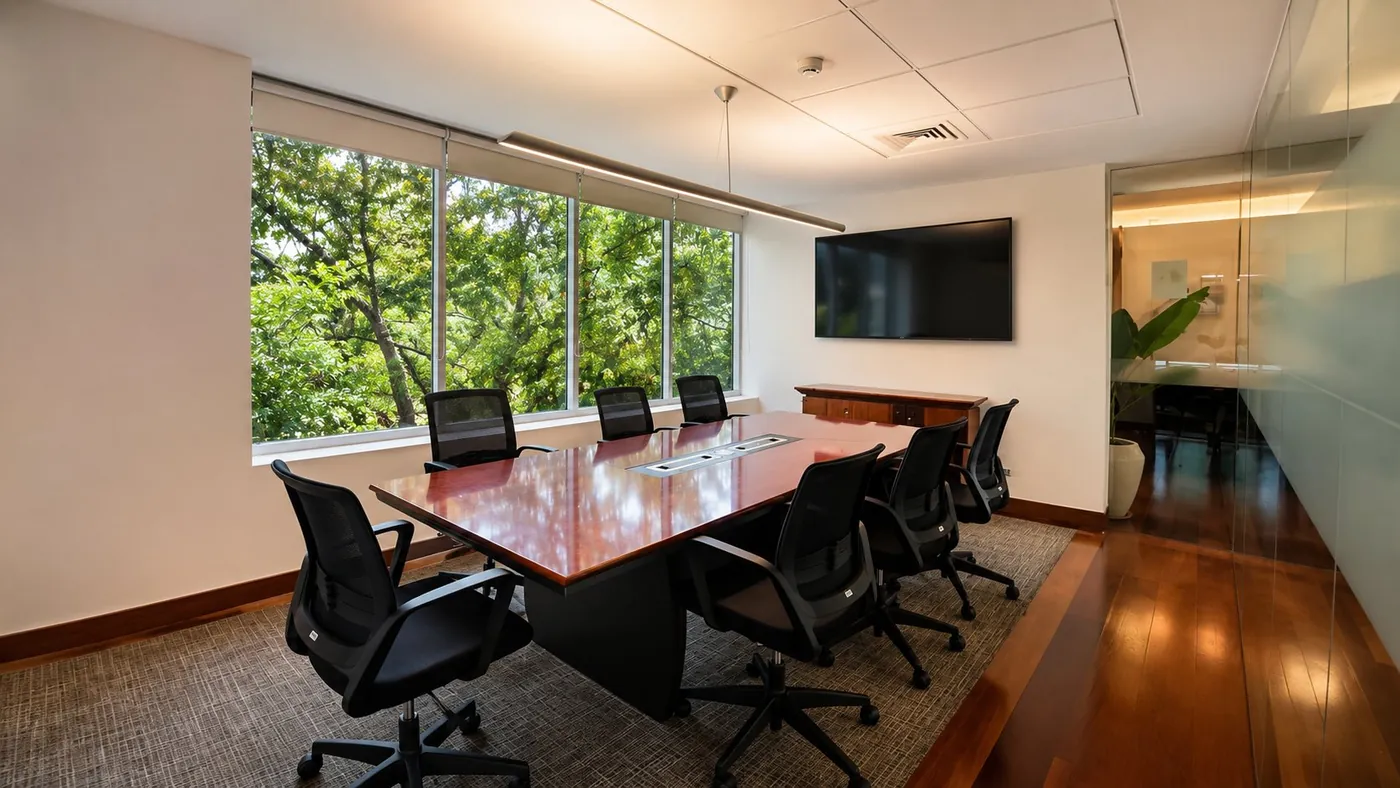 Sala de reunión formal con mesa de directorio, pantalla y vista al parque